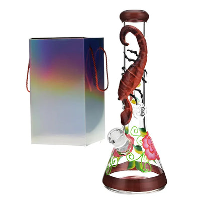 Glass smoking bong with a 3d scorpion and colourful base and floral accents, next to a rainbow-coloured box.